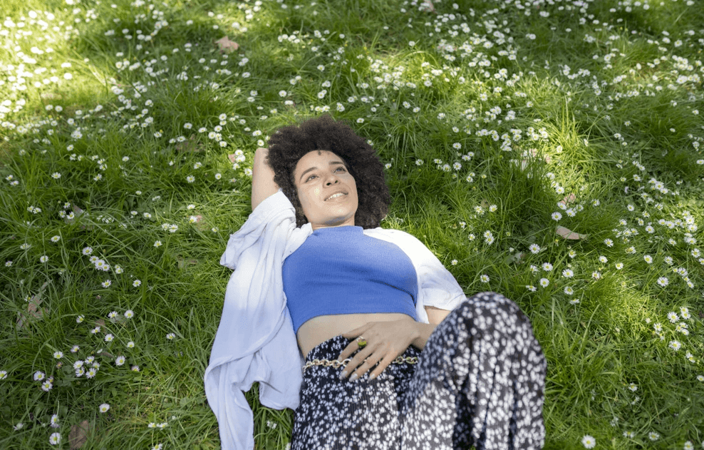 Woman laying on flowering grass looking up at the sky and thinking